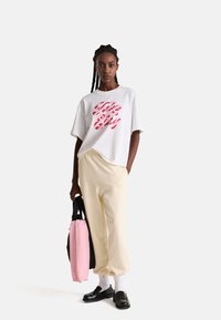 Camiseta blanca de gran tamaño con texto gráfico rosa, pantalones de chándal beige, mocasines negros y un bolso negro con un acento de tela rosa.