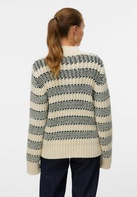 Jauktas megztinis grietinėlės ir juodų juostelių, su aukštu kaklu, įribuotais rankogaliais ir laisvu prigludimu. Textūruota siūlai akcentuoja raštą.