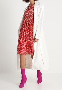 Červené květinové šaty s přiléhavým vrškem a rozšířenou sukní, překryté dlouhým bílým kabátem. Nejlepší s fuchsiovými kotníkovými botami.