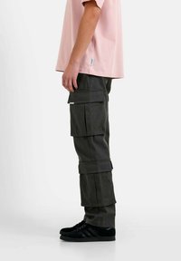Cargo-broeken in donkergrijs stof hebben meerdere grote zakken en een losse pasvorm. Gecombineerd met een lichtroze t-shirt en zwarte sneakers.