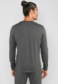 Langærmet grå skjorte lavet af blødt stof med rund hals og tætsiddende pasform. Bagsiden viser en glat tekstur og lange ærmer.