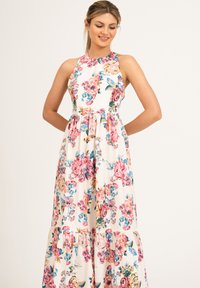 Sukienka maxi w kwiaty z wysokim dekoltem, bez rękawów, na białej podstawie, z dużymi różowo-niebieskimi wzorami kwiatowymi oraz falbaną na dole.