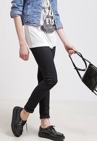 Svarta skinny jeans, vit t-shirt med grafik, jeansjacka, och svarta skor med ett strukturerat mönster. Svart handväska i handen. Avslappnad outfit.