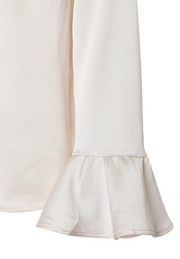 Light beige blouse with long sleeves, featuring a flared cuff detail. Smooth texture with a slight sheen, made from a lightweight fabric.