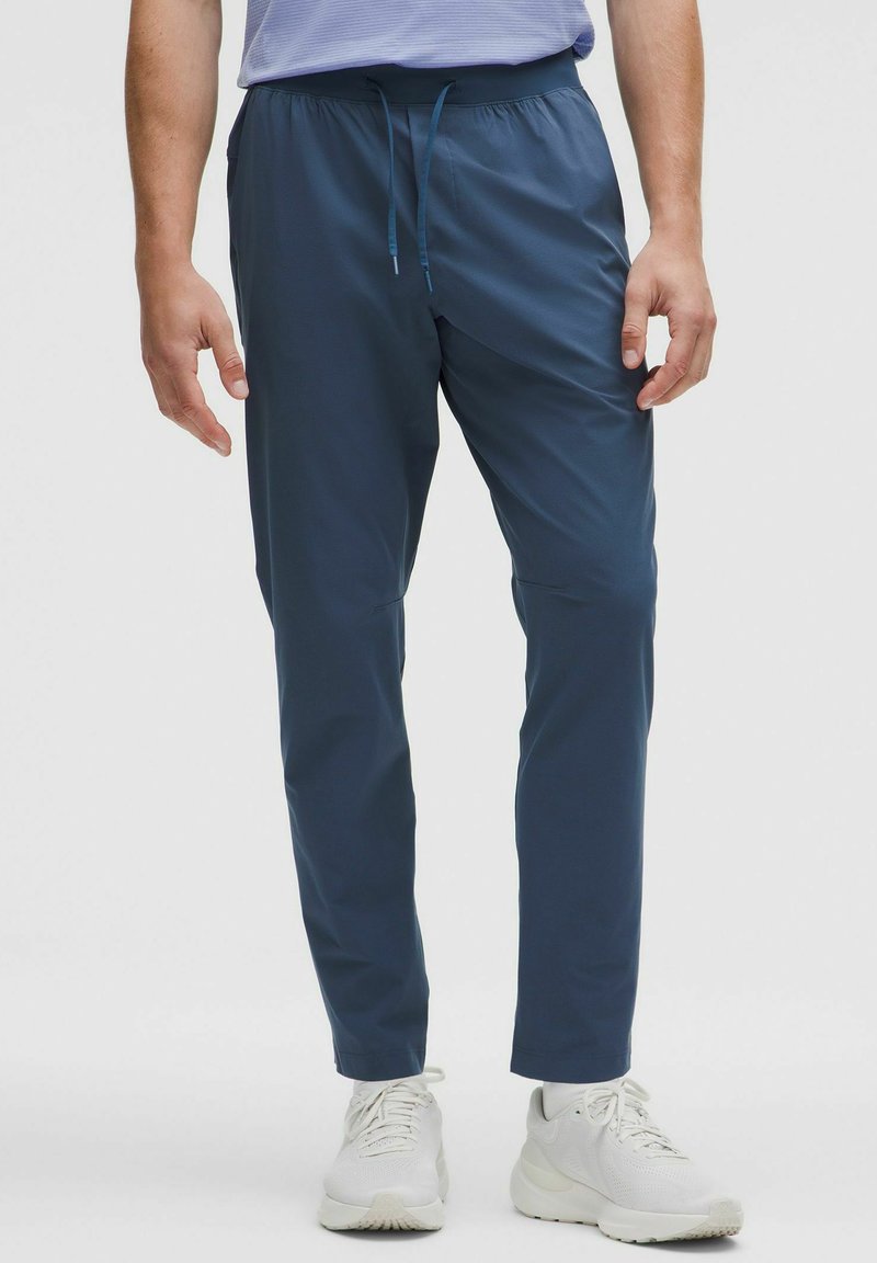 Herren tapered Hose in Dunkelblau, aus leichtem Stoff gefertigt. Sie verfügt über einen elastischen Bund mit Kordelzug und seitlichen Taschen.