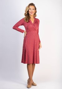 Punainen kuviollinen mekko, jossa on pitkät hihat, V-pääntie ja levenevä helma. Yhdistetty nudenvärisiin korkokenkiin, joissa on kultaiset yksityiskohdat. Sileä kangastuntu.