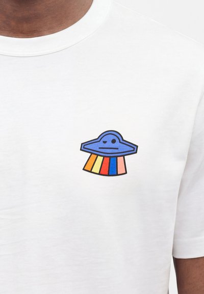 Λευκό μπλουζάκι με μικρό μπλε γραφικό UFO που εκπέμπει κάθετες ρίγες σε πορτοκαλί, κίτρινο, κόκκινο, μπλε και ροζ στο στήθος.
