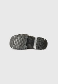 Sole di scarpa in gomma nera con scanalature profonde, caratterizzata da un motivo testurizzato per la presa e la durata. Il tallone è leggermente sollevato per un supporto migliore.