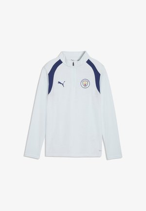 Biały sportowy top z długim rękawem z granatowymi paskami na ramionach, logo Manchester City na piersi, logo Puma i półzamkiem z przodu kołnierza.