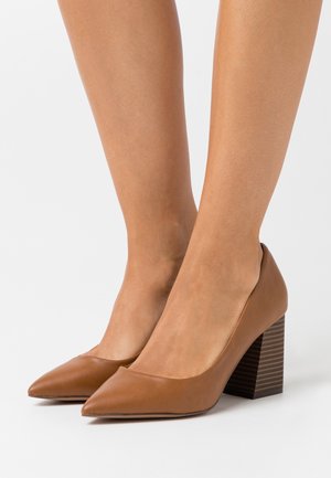 Chaussures à talons hauts en cuir brun avec un bout pointu et un talon bloc rayé épais, présentant une texture lisse et un design minimaliste.