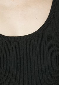 Detailní záběr na horní část hrudníku a výstřih osoby, která má na sobě černý úpletem šitý oděv s kulatým výstřihem.