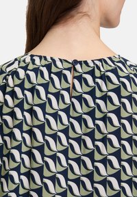 Granatowa bluzka z wzorem liści w zieleni i bieli, z zapięciem na guziki z tyłu oraz marszczonym dekoltem dla swobodnego kroju.