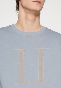 Felpa azzurra chiara con scollo a costine e grande logo ricamato "II" beige sulla parte anteriore.