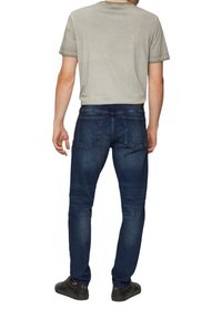 Camiseta gris de manga corta combinada con unos pantalones vaqueros ajustados azul oscuro, que cuentan con cinco bolsillos y una textura de denim desgastado. Unos zapatos negros completan el conjunto.