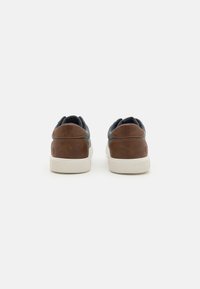 Brown and gray sneakers with a textured leather heel and suede upper, featuring a white rubber sole and a simple design.