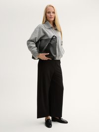 Grau strukturiertes Zip-Front Jacket, schwarze weit geschnittene Hose, schwarze Loafers und eine große schwarze Handtasche mit Schulterriemen und Reißverschluss.