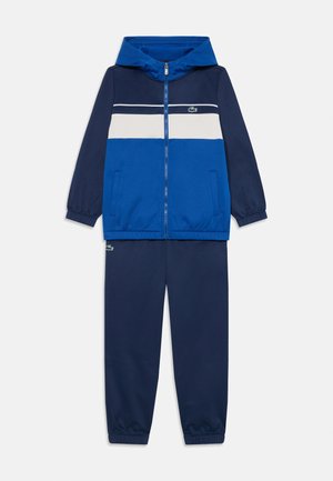 Blauwe sportieve trainingsoutfit met een ritsjack met capuchon, contrasterende strepen en bijpassende broek met elastische boorden, gemaakt van zachte stof.