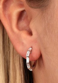 Silver hoopörhänge med rektangulära klara stenar, slät yta och en modern design, fotograferat i en närbild av ett öra.