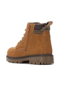 Bota de ante marrón con suela robusta, cremallera lateral, collar acolchado y acentos marrones. Presenta costuras en contraste y una construcción duradera.