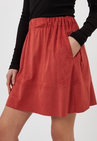 Jupe rouge texturée avec une taille élastique, des poches latérales et une silhouette évasée. Tissu lisse et doux avec un détail de couture près de l'ourlet.