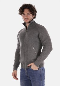 Maglione grigio a coste con zip e colletto alto, dotato di due tasche laterali e dettagli in zip argentati. Tessuto morbido, adatto per look informali.