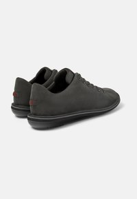 Sneakers in suede grigio con un design a profilo basso, dotati di sei occhielli, una suola in gomma nera testurizzata e un piccolo accento rosso con il logo sul tallone.