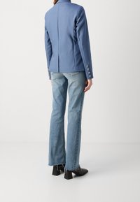 Blå skräddarsydd kavaj med ventilerad rygg, silvriga knappdetaljer på ärmarna, i kombination med utsvängda ljus denimjeans och svarta klackskor.