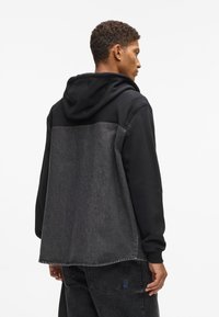 Μαύρη κουκούλα με πάνελ από τζην στο πίσω μέρος. Μαλακό ύφασμα, άνετη εφαρμογή και αντίθετες ραφές. Περιλαμβάνει τσέπη καγκουρό και ραμμένα μανίκια.