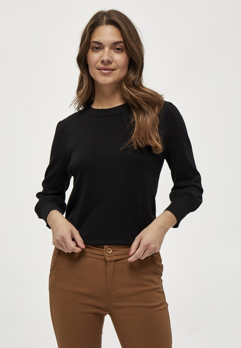 Svart stickad tröja med rund halsringning och lång puffärm, kombinerad med bruna höga byxor med bälte och texturerat tyg.
