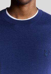 Maglione blu navy a girocollo realizzato in tessuto lavorato a maglia, con un piccolo logo ricamato sul petto e un colletto interno bianco a contrasto.