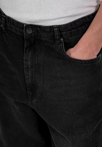 Los pantalones vaqueros de mezclilla negra presentan un diseño clásico con un corte relajado, bolsillos delanteros y una cinturilla con un botón de metal.