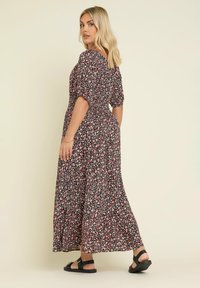 Blommig midiklänning med korta ärmar, svart bas, rosa och vita blommor, rynkad midja, flödande kjol, kombinerad med svarta sandaler.