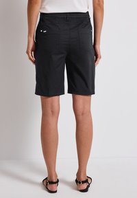 Pantalones cortos negros con una cintura de altura media, cuatro bolsillos y una tela lisa y texturizada. La parte trasera cuenta con un sutil detalle del logo y costuras en contraste.