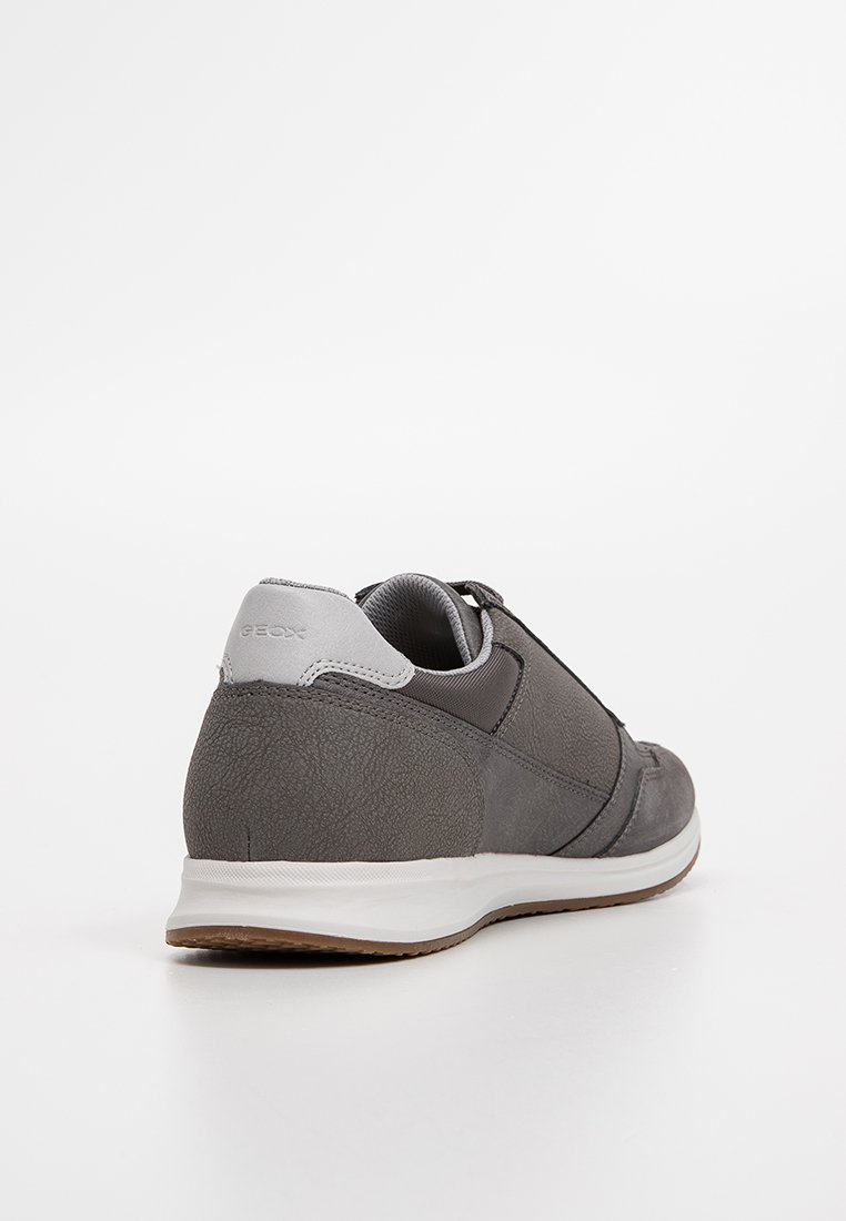 Sneaker gris avec un mélange de matériaux lisses et texturés, présentant un accent de talon gris, une semelle blanche et un design minimaliste.