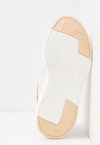 Valkoisen lenkkarin pohja, jossa on teksturoitu pito, beige ja vaaleanpunainen korostus. Koko 37 merkitty pohjaan.