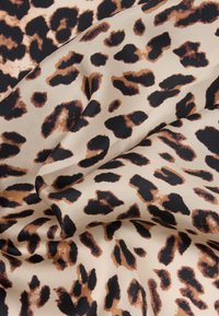 Μπεζ ύφασμα με λεία υφή διακοσμημένο με ακανόνιστα μαύρα και καφέ λεκέδες λεοpard, ελαφρώς διπλωμένο.