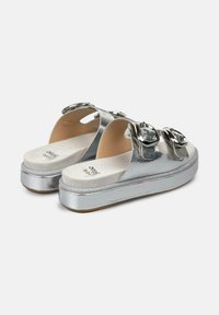 Zilveren metallic slide sandalen hebben een glanzende afwerking, twee grote circulaire accenten en een gestructureerde zool voor grip. Het platformontwerp voegt hoogte toe.
