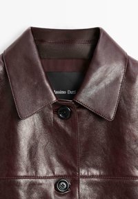 Bordeauxfarbene Lederjacke mit breitem Kragen, einreihiger schwarzer Knopfverschluss und sichtbaren Nähdetails. Das Innenschild trägt die Aufschrift "Massimo Dutti."