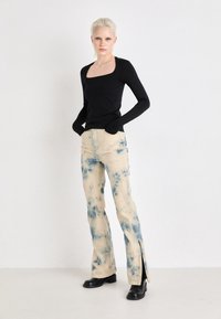 Svart langermet topp med firkantet utringning, kombinert med lysfarget denim bukser med blå tie-dye-mønster og sideslister. Svart ankelstøvler.