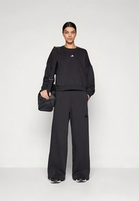 Μαύρο αθλητικό σύνολο που περιλαμβάνει cropped φούτερ με μικρό λογότυπο και φαρδιά παντελόνια. Το αξεσουάρ είναι μια μαύρη τσάντα χιαστί.