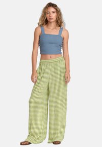 Blå texturerad crop top med breda axelband; lösa gröna och vita rutiga palazzo byxor; bruna sandaler; enkel vit bakgrund.