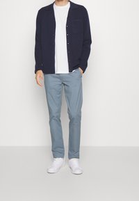 Marineblå skjorta med knappar, vit t-shirt under, ljusblå byxor och vita sneakers. Slätt tyg, avslappnad design med en fickdetalj.