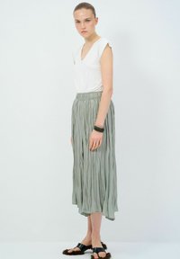 Gonna midi plissettata leggera grigia con vita elasticizzata, abbinata a una maglietta bianca a scollo a V e scarpe in stile sandalino nere. Tessuto liscio e fluido.
