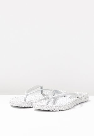 Par hvide teksturerede flip-flops med glitrende stropper på en hvid overflade og lys grå baggrund.