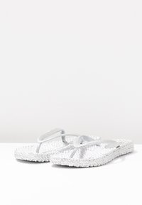 Vita flip-flops med texturerade, vävda sulor och glänsande, silverfärgade tvärband. Lämpliga för avslappnad sommaranvändning.