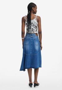 Denimrock mit ausgestelltem Saum, heller Waschung und zwei Gesäßtaschen, kombiniert mit einem gemusterten Cropped-Top mit verstellbaren Bindebändern.