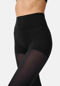 Hochtaillierte schwarze Leggings verfügen über ein glattes, undurchsichtiges Oberteil mit einem durchsichtigen Einsatz am unteren Bein, gefertigt aus dehnbarem Material für Komfort.