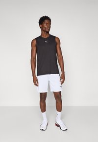 Svart ermeles topp i atletisk stil med en tettsittende design, kombinert med hvite shorts. Antrekket fullføres med hvite sneakers med svarte detaljer.