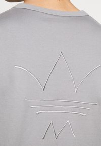 T-shirt in cotone grigio con un design ricamato bianco di una corona e linee sul retro, dotato di scollatura a coste.