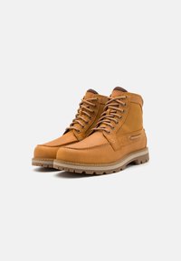 Botas de couro castanho com um design de tornozelo alto, bico redondo e atacadores castanhos. Apresentam um forro texturizado em castanho e uma sola robusta para melhor tração.